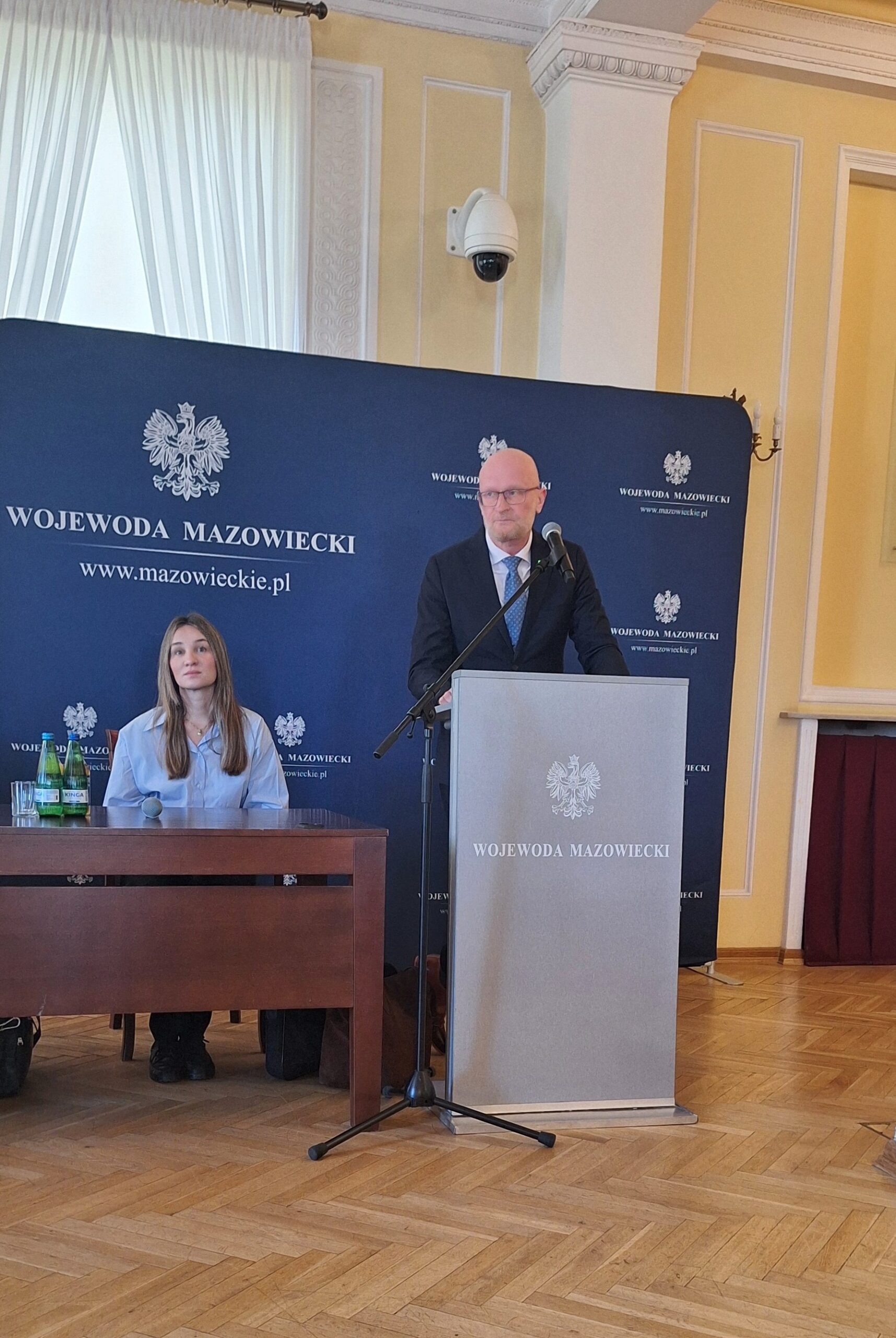 Zdjęcie przedstawia Głównego Geodetę Kraju przy mównicy oraz siedzącą Dyrektor Departamentu Nadzoru i Kontroli Adriannę Berenson